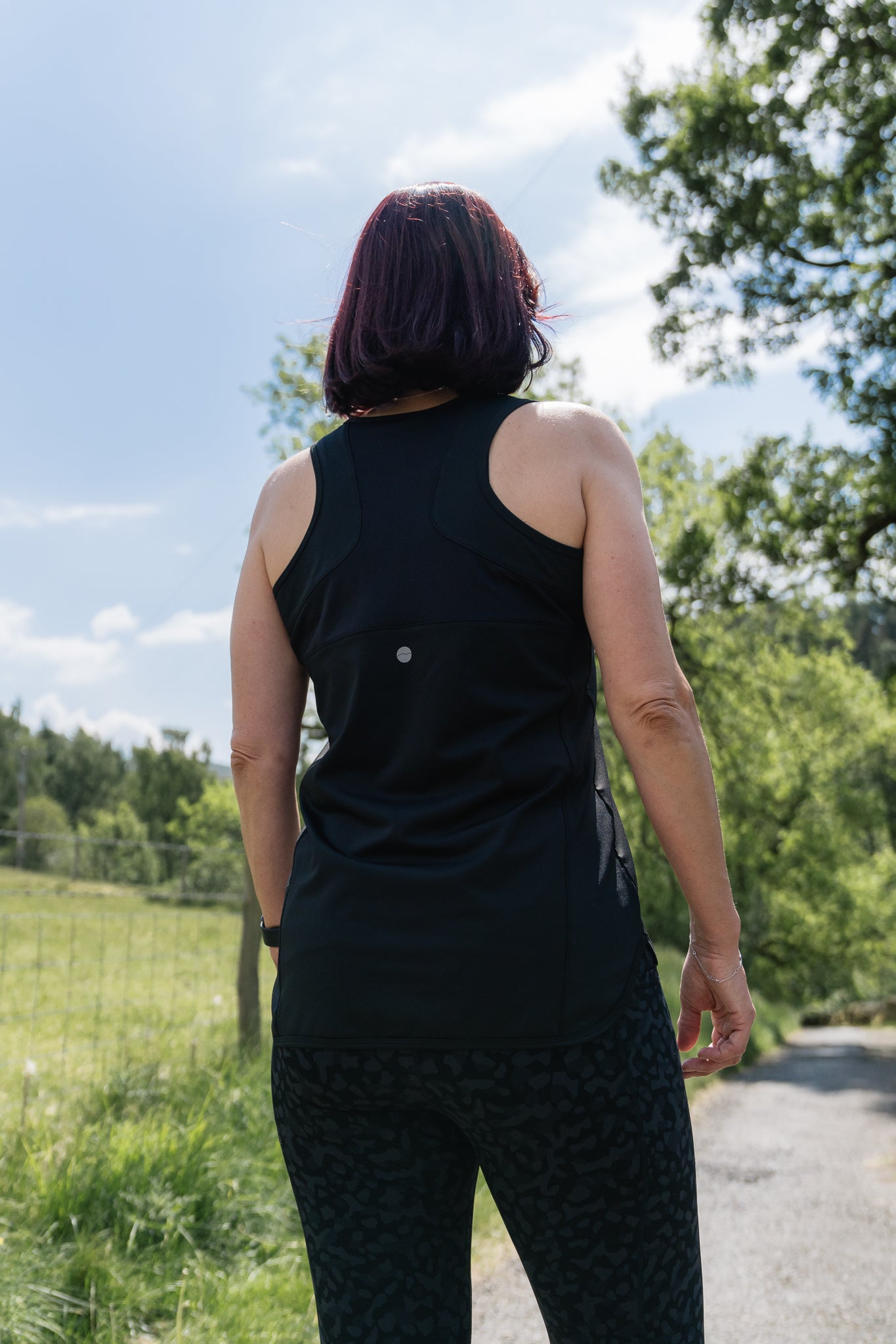 Person wearing a black sleeveless top and patterned pants standing outdoors with trees and sky in the background