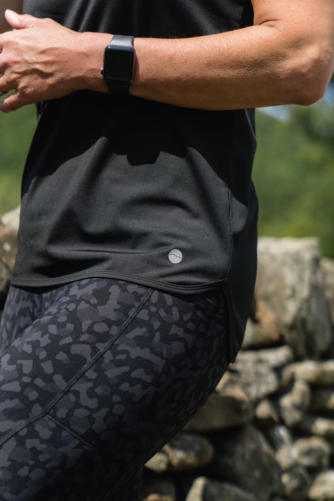 Person wearing a black athletic outfit with a patterned design, standing against a stone wall.