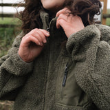 A woman wearing a khaki borg zip-through fleece with funnel neck and elasticated hem, featuring two large hand pockets and one small zipped chest pocket.