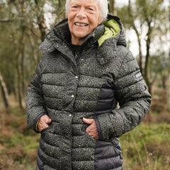 A person wearing a hooded khaki print puffer jacket with vibrant lime accents, featuring hand pockets and a detachable hood.