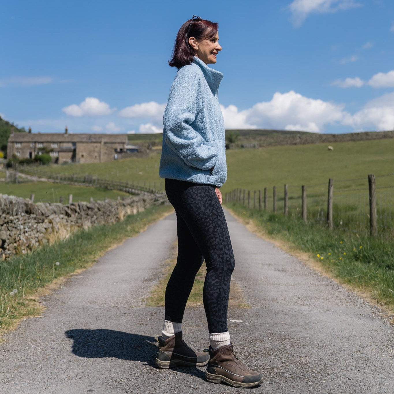 Person standing on a path in a rural landscape with a clear blue sky.