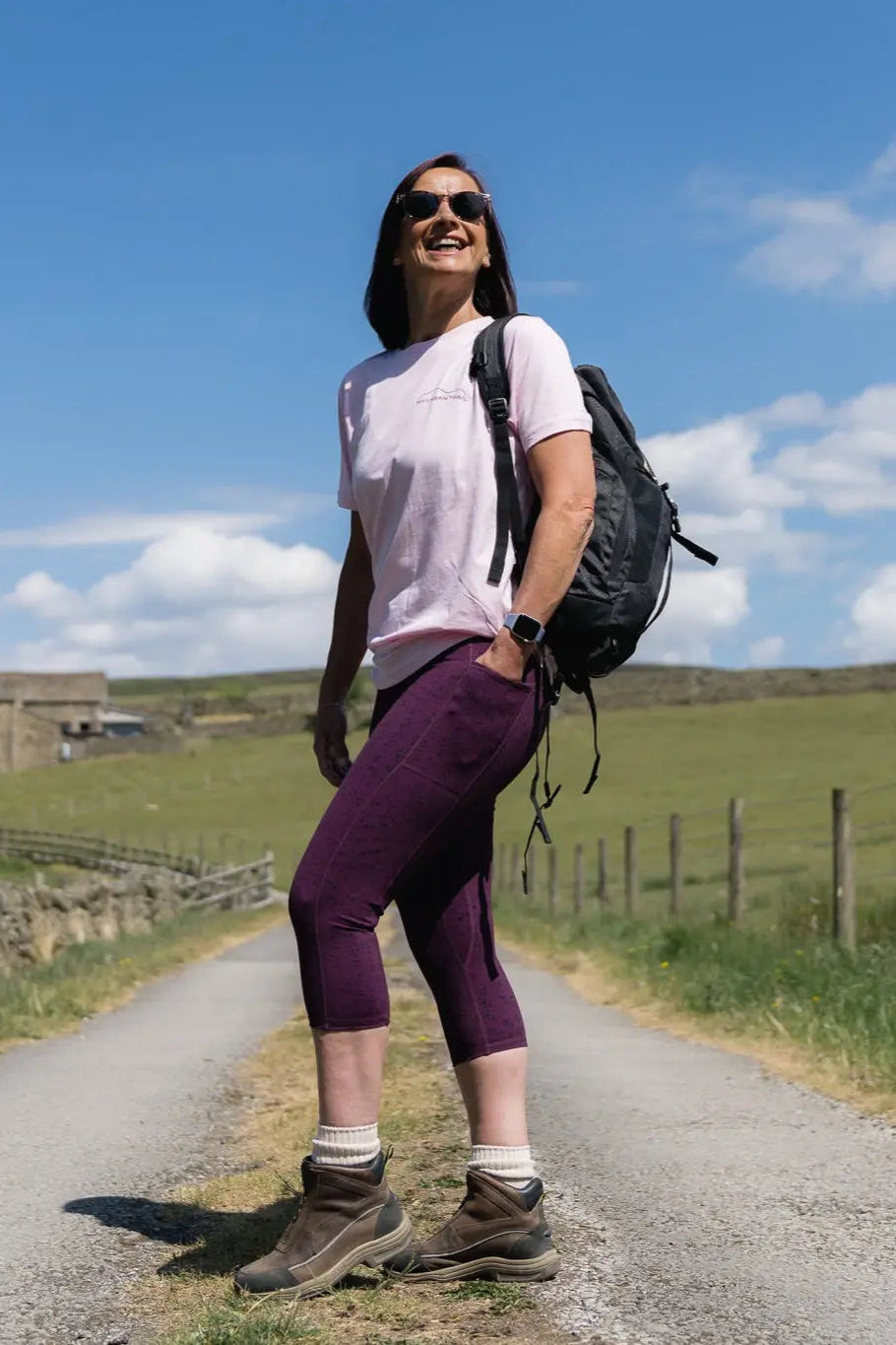 Woman with a backpack standing on a rural road under a blue sky.