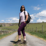 Woman with a backpack standing on a rural road under a blue sky.