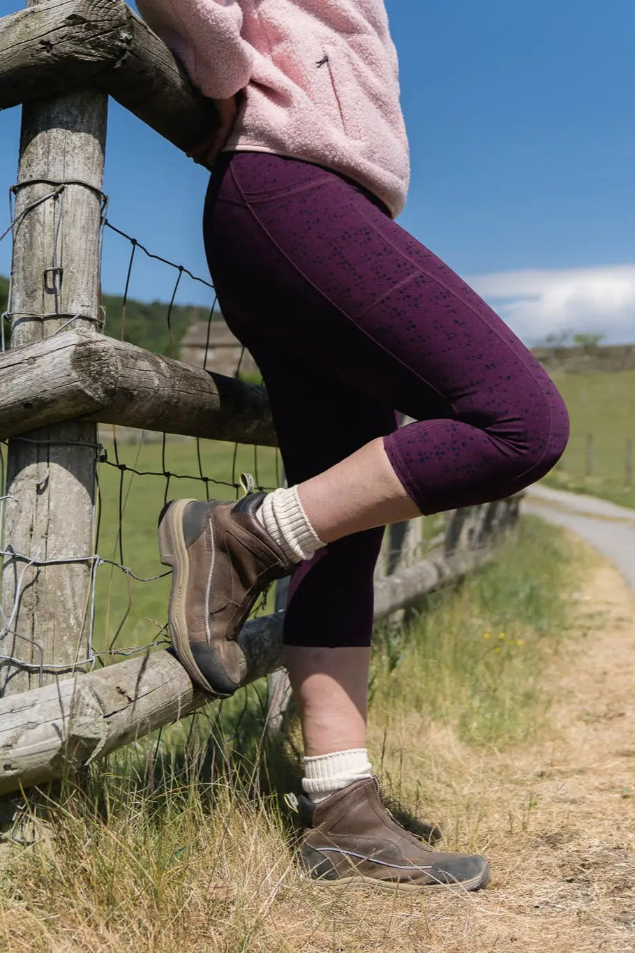 Person sitting on a wooden fence by a rural road with a clear blue sky.
