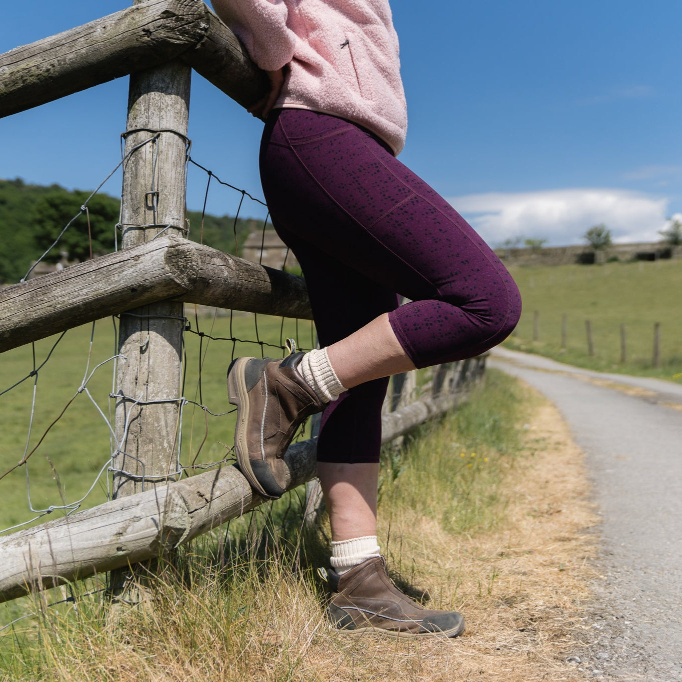 Person sitting on a wooden fence by a rural road with a clear blue sky.