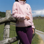 Woman in a pink jacket standing by a wooden fence with a clear blue sky.
