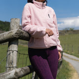Woman in a pink jacket standing by a wooden fence with a clear blue sky.