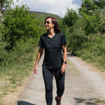 Woman walking on a dirt path in a natural setting with trees and mountains in the background.