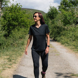 Woman walking on a dirt path in a natural setting with trees and mountains in the background.