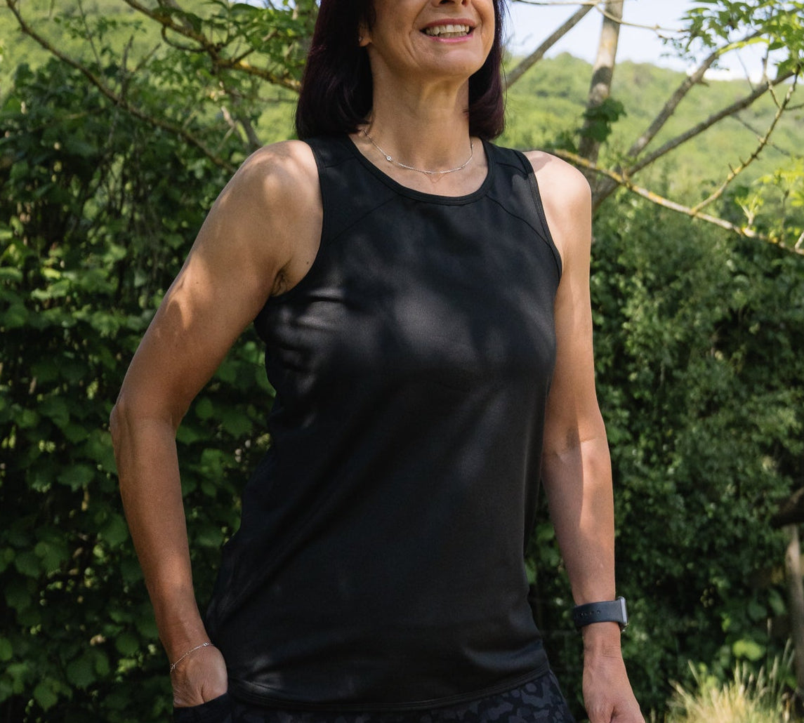 Woman wearing a black tank top and sunglasses standing outdoors with greenery in the background