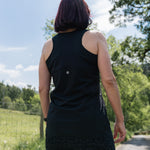 Person wearing a black sleeveless top and patterned pants standing outdoors with trees and sky in the background