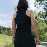 Person wearing a black sleeveless top and patterned pants standing outdoors with trees and sky in the background
