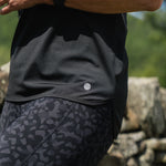 Person wearing a black athletic outfit with a patterned design, standing against a stone wall.