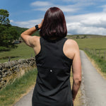 Person in a black sleeveless sports top standing on a country road with green fields and trees in the background.