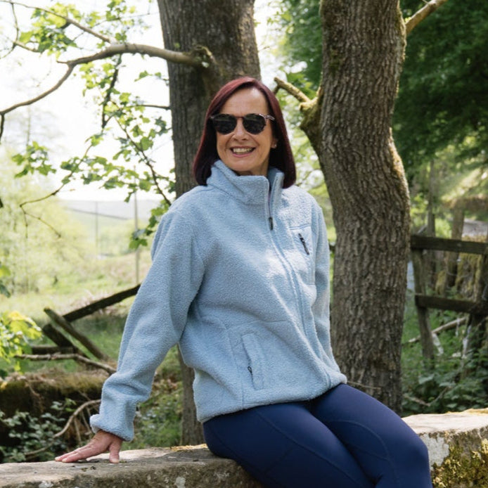 Woman in a light blue fleece jacket sitting outdoors near trees