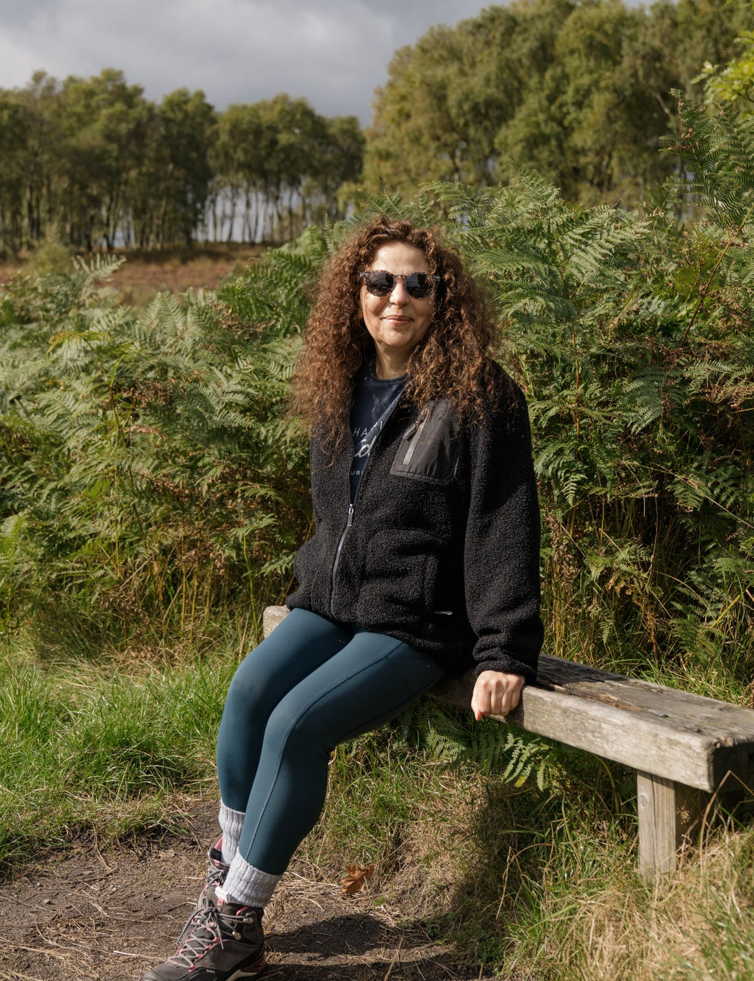 Person sitting on a wooden bench in a natural setting with trees and grass.