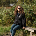 Person sitting on a wooden bench in a natural setting with trees and grass.