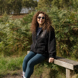 Person sitting on a wooden bench in a natural setting with trees and grass.