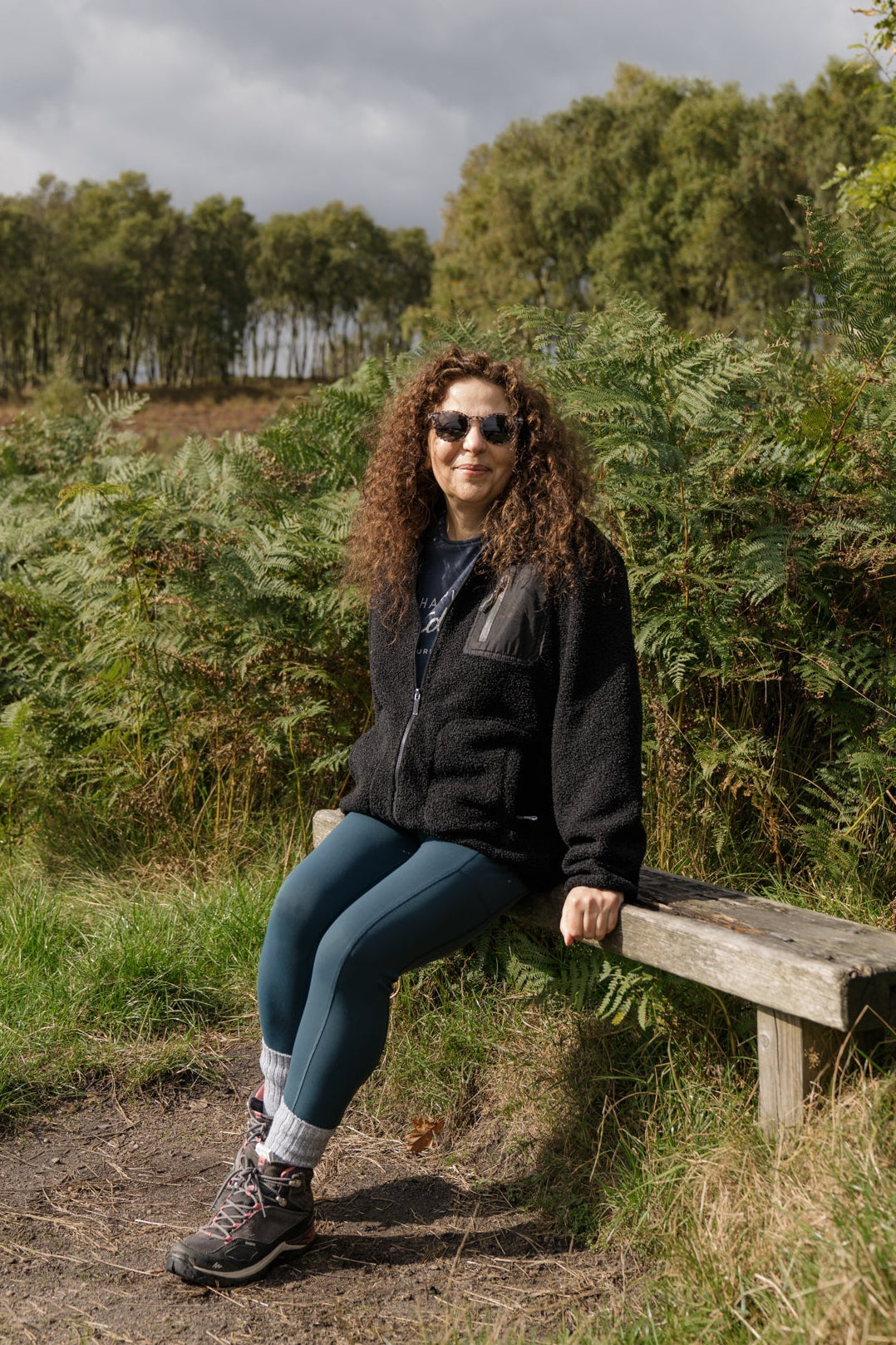 Person sitting on a wooden bench in a natural setting with trees and grass.