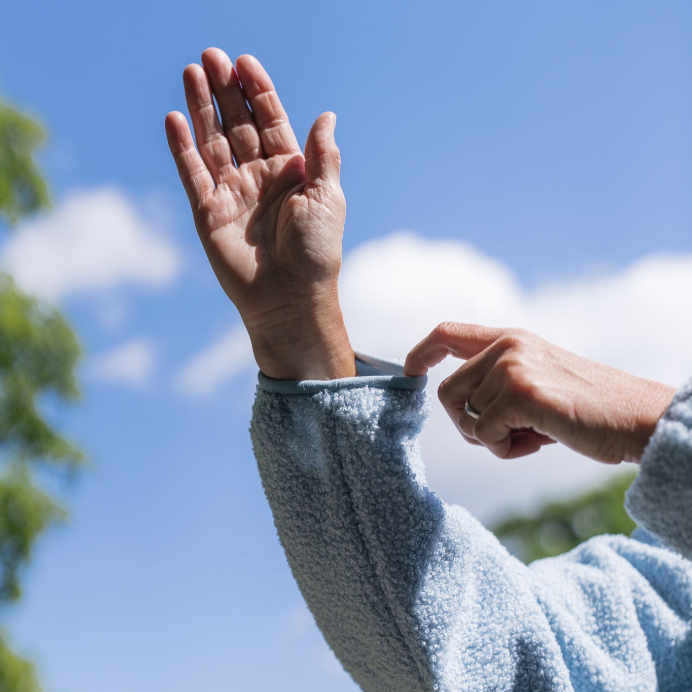 Person wearing a light blue sweater against a clear blue sky with trees in the background